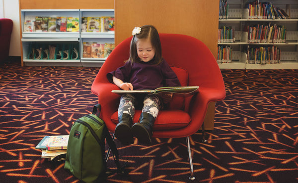 A child reading with The Sprout on the ground next to their chair.